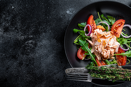 Salad with baked salmon fillet steak, fresh arugula and tomato in a plate. Black background. Top view. Copy space.
