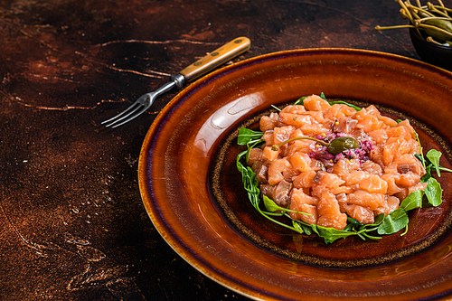 Tartar or tartare with salmon fish, red onion, arugula and capers in rustic plate. Dark background. Top View. Copy space.