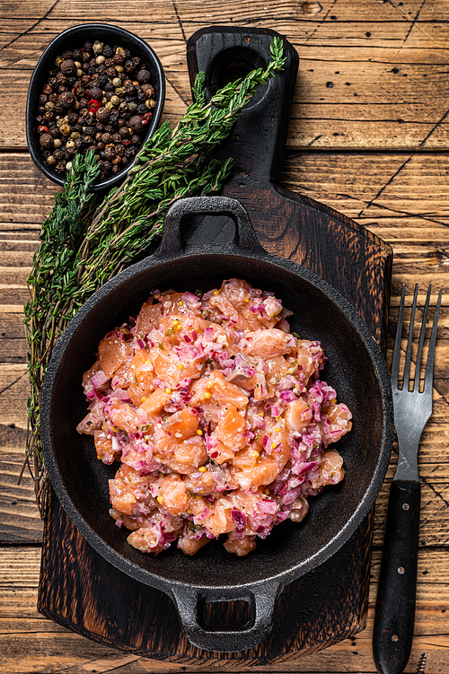 Tartar or tartare with salmon fish, red onion, arugula and capers in a pan. Wooden background. Top View.