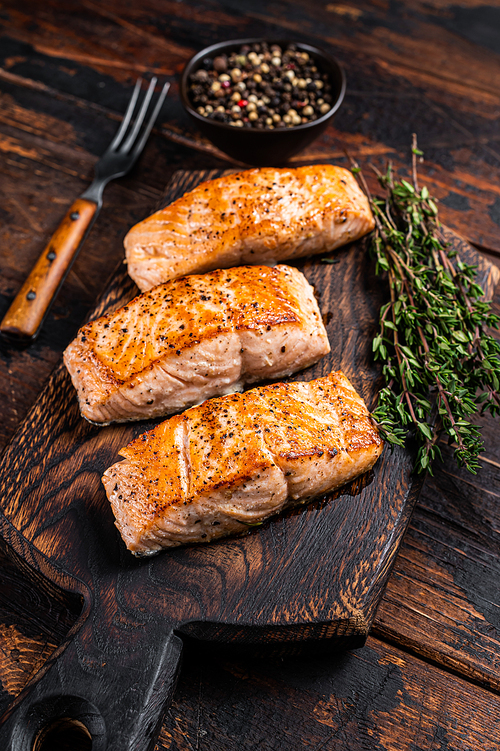 Fried Salmon Fillet Steaks on a wooden board with thyme. Dark wooden background. Top view.