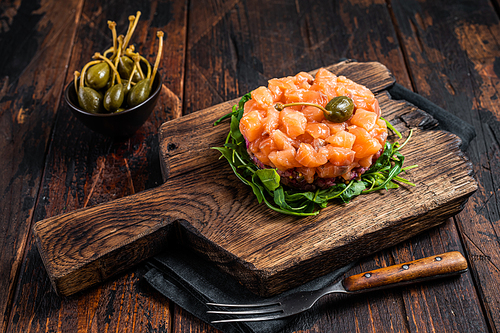 Salmon tartare or tartar with red onion, avocado, arugula and capers. Dark wooden background. Top View.
