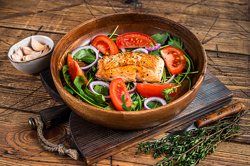 Salmon steak salad with green leaves arugula, avocado and tomato in a wooden plate. Wooden background. Top view.