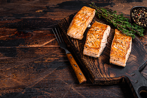 Fried Salmon Fillet Steaks on a wooden board with thyme. Dark wooden background. Top view. Copy space.