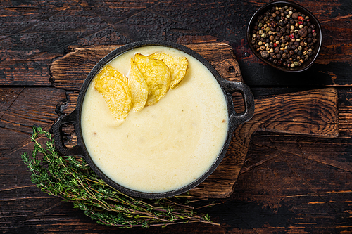 Potato cream soup with potato chips in pan on wooden board. Dark wooden background. Top view.