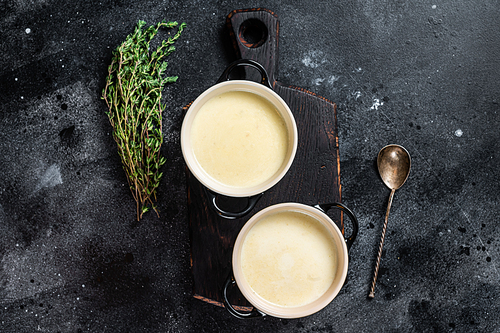 Potato cream soup in bowls on kitchen table. Black background. Top view.