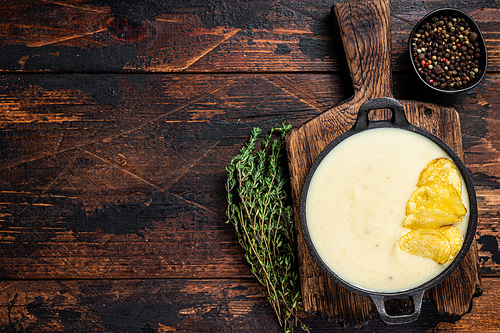 Potato cream soup with potato chips in pan on wooden board. Dark wooden background. Top view. Copy space.