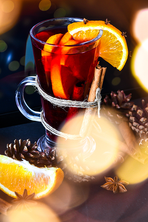 Mulled wine Hot christmas drink with spices on a dark background. Orange slices, cinnamon sticks, christmas cones, bright bokeh. Christmas light. Holiday atmosphere, Rustic style. The idea for creating greeting cards