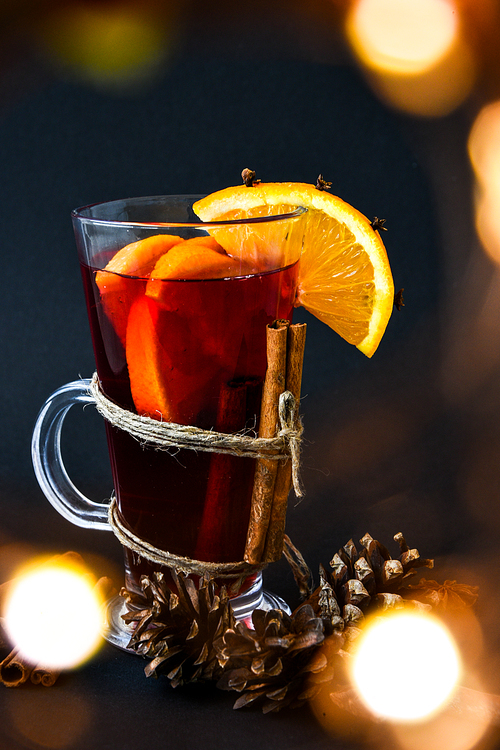 Mulled wine Hot christmas drink with spices on a dark background. Orange slices, cinnamon sticks, christmas cones, bright bokeh. Christmas light. Holiday atmosphere, Rustic style. The idea for creating greeting cards