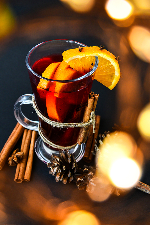 Mulled wine Hot christmas drink with spices on a dark background. Orange slices, cinnamon sticks, christmas cones, bright bokeh. Christmas light. Holiday atmosphere, Rustic style. The idea for creating greeting cards