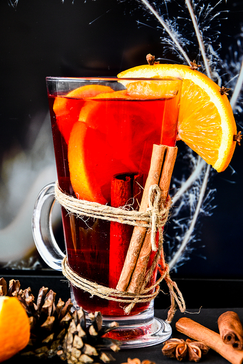 Mulled wine Hot christmas drink with spices on a dark background. Orange slices, cinnamon sticks, christmas cones, bright bokeh. Holiday atmosphere, Rustic style. The idea for creating greeting cards