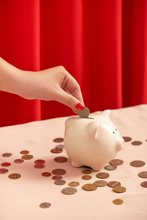 A female hand hold a coin and insert into pig coin bank