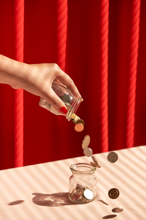 A female hand hold a coin and insert into glass jar