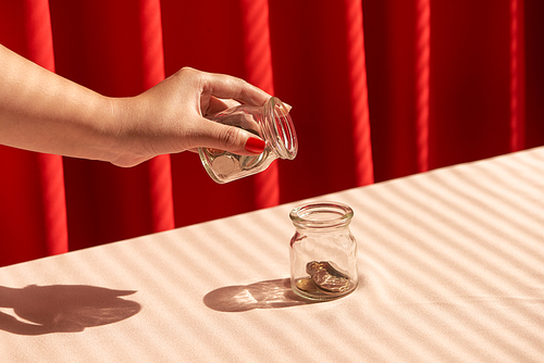 A female hand hold a coin and insert into glass jar