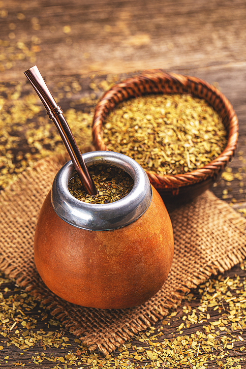 South American yerba mate tea in calabash with bombilla and dried leaves in wooden bowl