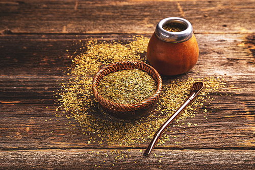 Calabash and bombilla with yerba mate on wooden background