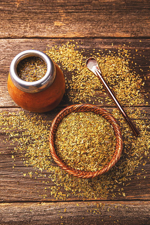 Yerba mate in calabash and dry herb in wooden bowl on wooden background. Top view