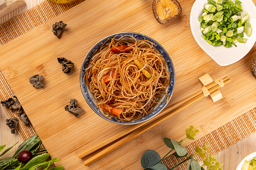Flat lay of bowl of noodles with carrots on bamboo background