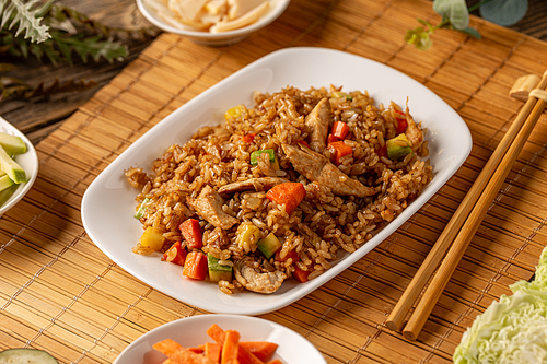 Fried rice with chicken served in a white plate on bamboo tablecloth