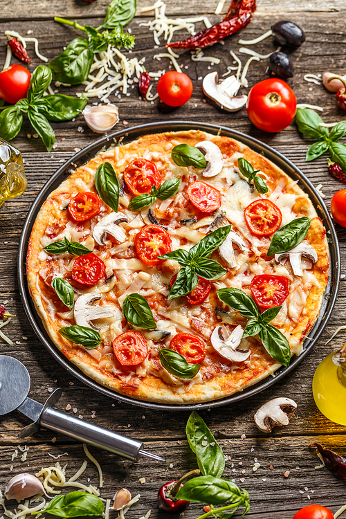Pizza decorated with basil leaves served in metal tray on wooden background