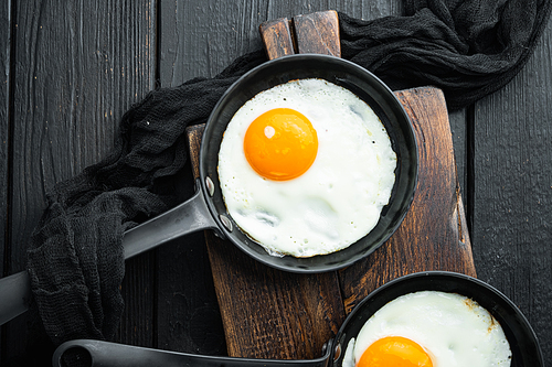 Fried eggs with cherry tomatoes and bread for breakfast in cast iron frying pan, on black wooden table background, top view flat lay