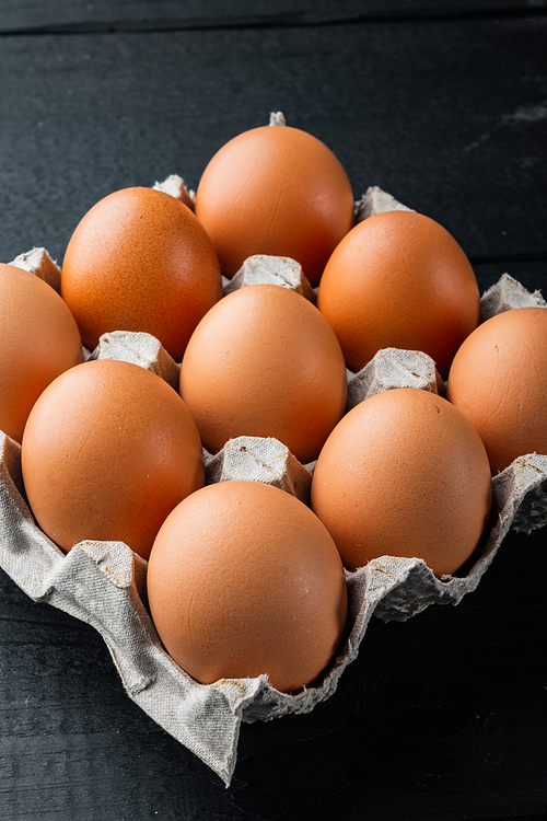 Raw chicken eggs in egg box set, on black wooden table background