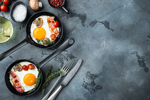 Fried eggs with cherry tomatoes and bread for breakfast in cast iron frying pan, on gray background, top view flat lay , with space for text copyspace