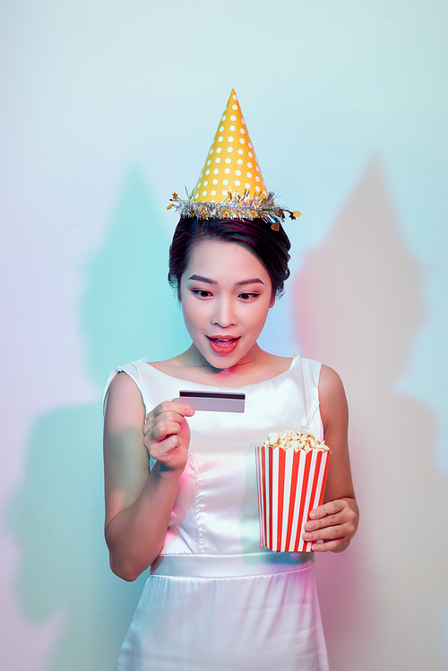 Portrait of young smiling attractive brunette woman in casual clothes watching movie film, holding bucket of popcorn and credit card isolated on white background. Emotions in cinema concept