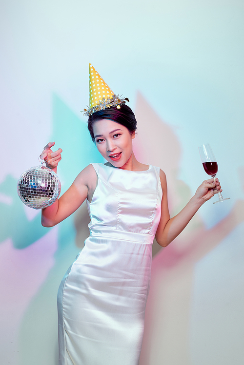 Portrait of a happy beautiful woman in white dress having a party and drinking champagne while standing with disco ball isolated over light background