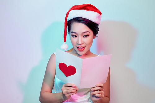 Beautiful happy asian woman in Santa Claus hat holding love letter with heart