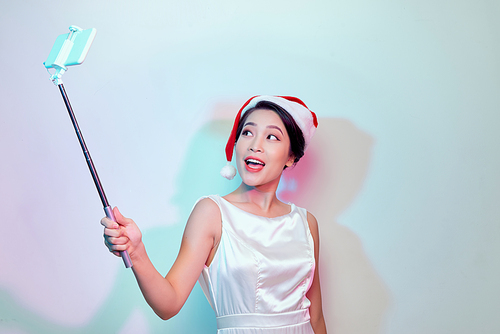 Beautiful happy asian woman in Santa Claus hat making selfie photo with phone