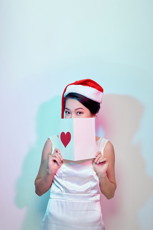 Beautiful happy asian woman in Santa Claus hat holding love letter with heart