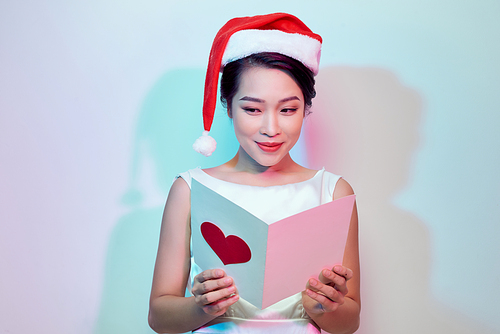 beautiful young woman holding a valentine postcard with a pink heart on light background