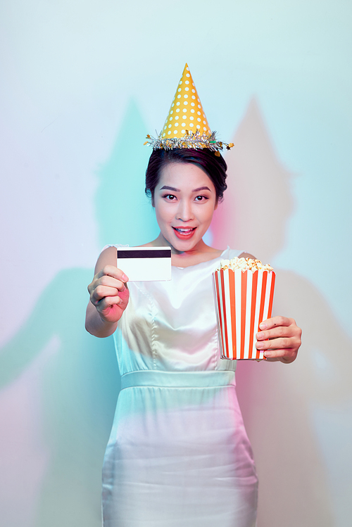 Portrait of young smiling attractive brunette woman in casual clothes watching movie film, holding bucket of popcorn and credit card isolated on white background. Emotions in cinema concept