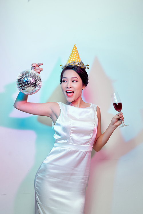 Portrait of a happy beautiful woman in white dress having a party and drinking champagne while standing with disco ball isolated over light background