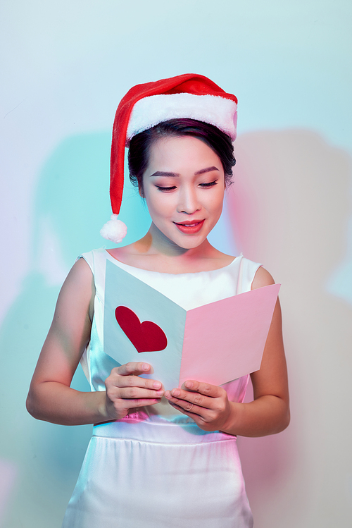 beautiful young woman holding a valentine postcard with a pink heart on light background