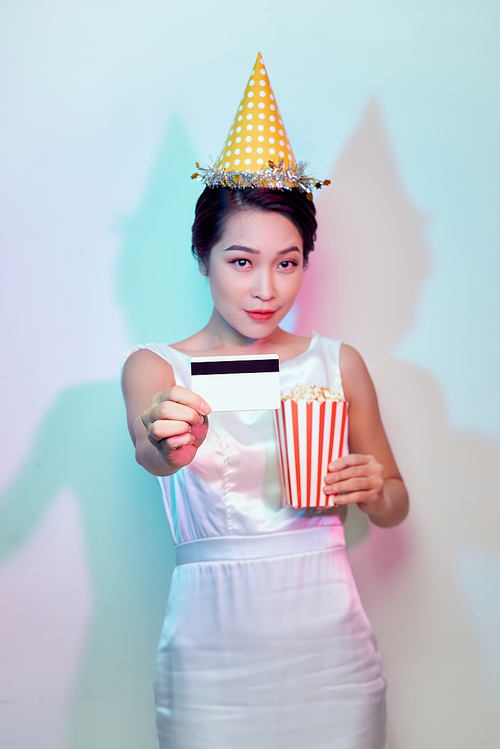 Portrait of young smiling attractive brunette woman in casual clothes watching movie film, holding bucket of popcorn and credit card isolated on white background. Emotions in cinema concept