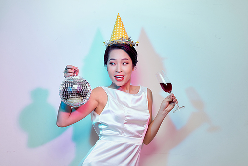 Portrait of a happy beautiful woman in white dress having a party and drinking champagne while standing with disco ball isolated over light background