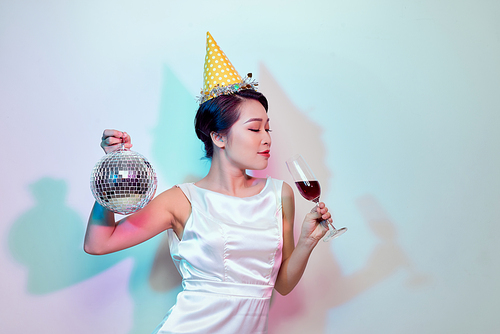 Portrait of a happy beautiful woman in white dress having a party and drinking champagne while standing with disco ball isolated over light background