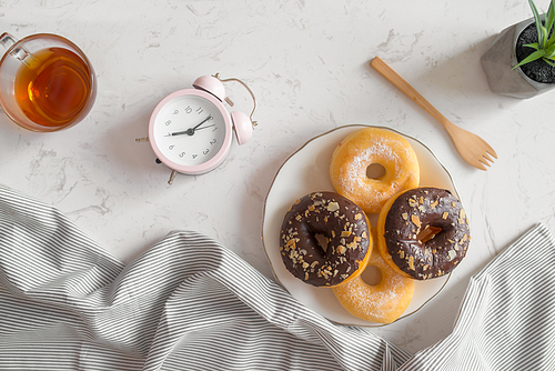 Top view of coffee cup with donut and clock on table. Morning breakfast.