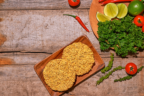 Raw asian instant noodles on wooden board with vegetables