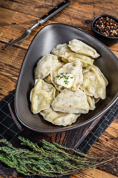 Dumplings pierogi with potato in a plate with herbs and butter. Wooden background. Top View.