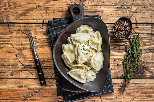 Dumplings pierogi with potato in a plate with herbs and butter. Wooden background. Top View.