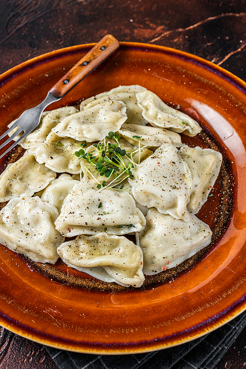 Polish Pierogi Dumplings with potato in a plate with herbs and butter. Dark background. Top View.