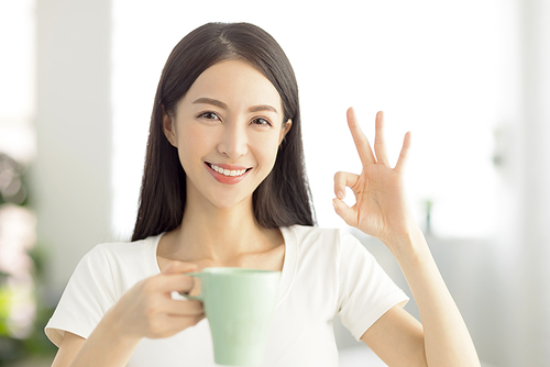 beautiful young woman holding a cup of tea and showing ok gesture
