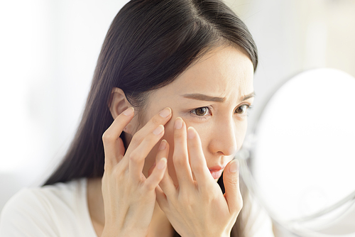 Young woman looking at  mirror and checking the  acne problem at home