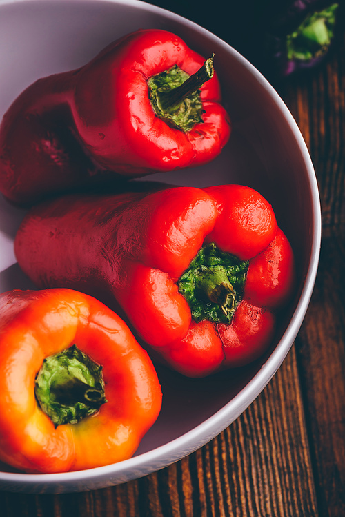 Multicolored fresh bell peppers in bowl over wooden background