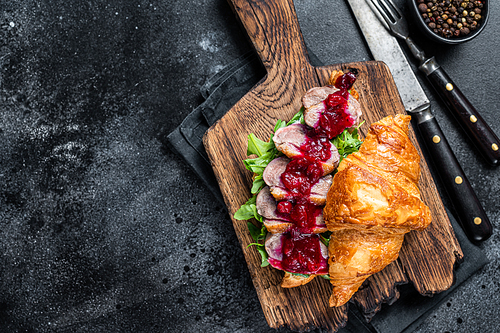 Croissant sandwich with Duck breast steak slices, arugula and sauce. Black background. Top View. Copy space.