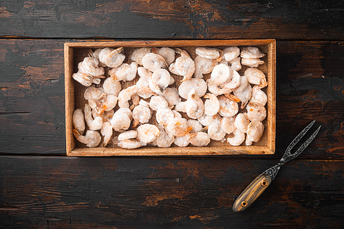 Pink frozen shrimps with ice. Uncooked peeled seafood set, in wooden box, on old dark  wooden table, top view flat lay, with copy space for text