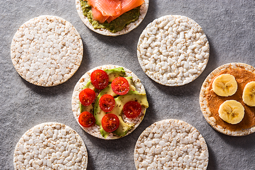 Puffed rice cakes with guacamole salmon,tomato and avocado, and banana with peanut butter on gray stone background