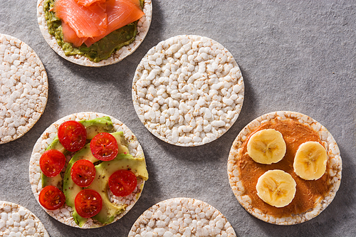 Puffed rice cakes with guacamole salmon,tomato and avocado, and banana with peanut butter on gray stone background